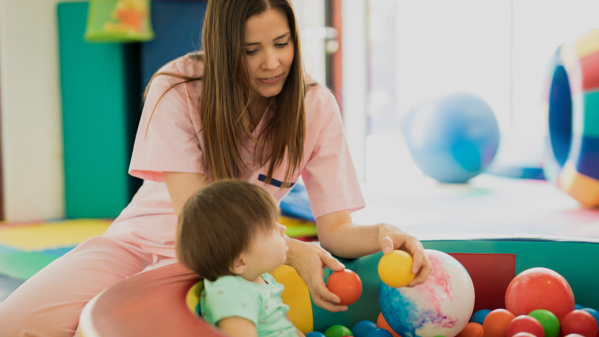 Childhood development center therapists - Pediatric therapist helping a toddler develop motor and sensory skills through colorful ball play.
