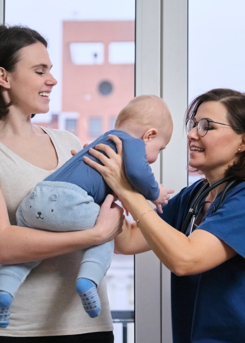 Early evaluation stimulation movil - Mother holding her baby during a pediatric consultation with a healthcare professional, supporting early childhood development.