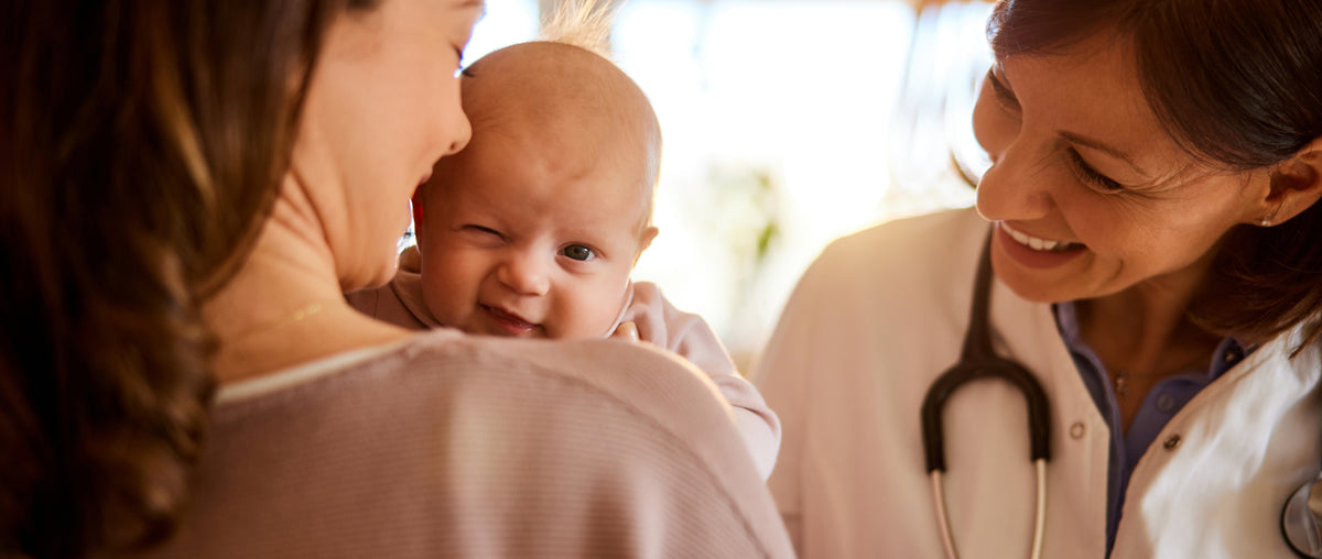 Early intervention program every - Pediatrician smiling at a baby held by their mother during a medical consultation.