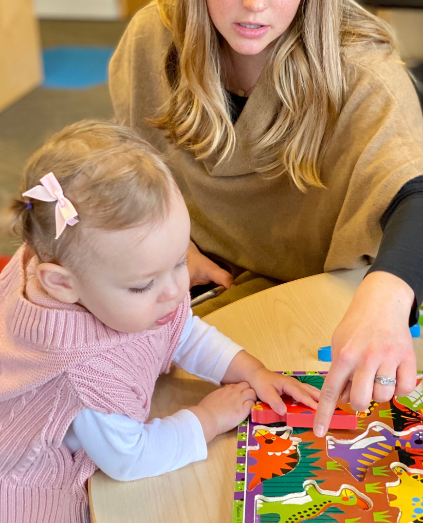 Early intervention program one - Woman guiding a toddler through a colorful educational puzzle during an early childhood learning activity.